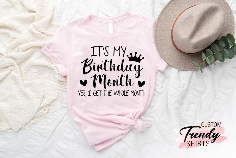 May include: Pink t-shirt with the text "It's My Birthday Month. Yes, I get the whole month." with a crown and hearts.