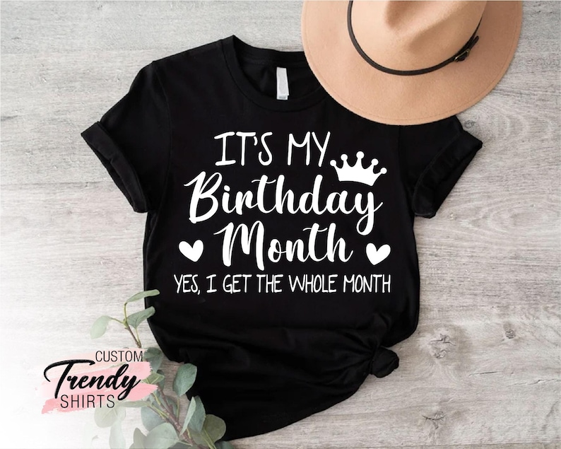 May include: Black t-shirt with white text that reads "It's My Birthday Month. Yes, I get the whole month."  A crown and two hearts are above the text.