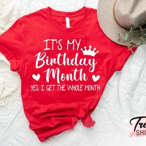 May include: Red t-shirt with white text that says "It's My Birthday Month. Yes, I get the whole month." with a crown and hearts.