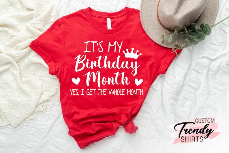 May include: Red t-shirt with white text that says "It's My Birthday Month. Yes, I get the whole month." with a crown and hearts.