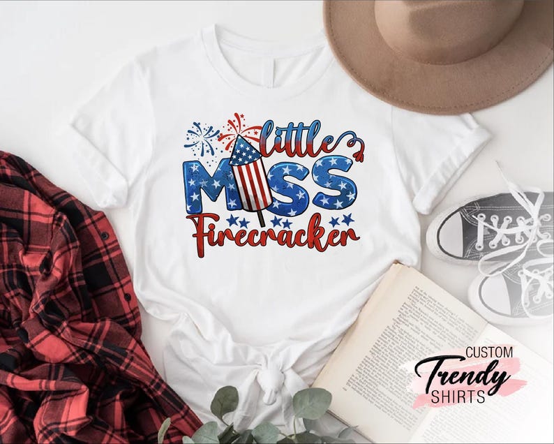 May include: White t-shirt with a red, white, and blue firework graphic and the text "Little Miss Firecracker".
