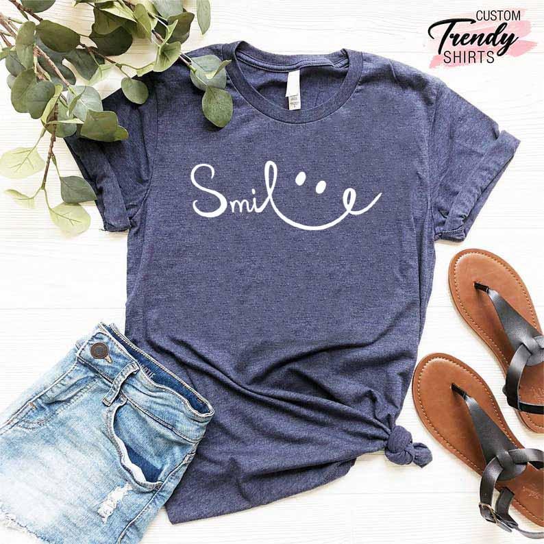 Op de afbeelding: Een marineblauw t-shirt met een witte afbeelding waarop 'Smile' staat met een smiley. Het shirt is gemaakt van een zacht, comfortabel materiaal en is perfect voor dagelijks gebruik.