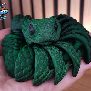 Puede incluir: Escultura verde oscuro de una serpiente con escamas detalladas y ojos grandes y oscuros. La serpiente está enrollada, con la cabeza levantada. Parece ser una impresión 3D. El logotipo "KOGI3D" es visible.