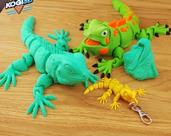 May include: A collection of 3D-printed iguana figurines in various sizes and colors. The largest is teal, the middle one is green with orange accents, and the smallest is yellow with a keychain clasp. The logo "KOGI3D" is in the top left corner.