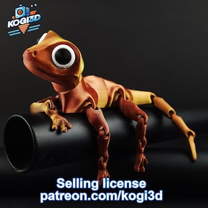Peut inclure: Une figurine de gecko articulée imprimée en 3D avec une coloration orange et jaune. Le gecko est posé sur un tuyau noir, les pattes tendues. La figurine a de grands yeux ronds.