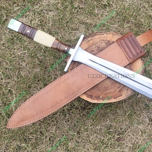 May include: A silver and brown dagger with a leather sheath. The dagger has a double-edged blade and a crossguard. The handle is wrapped in brown leather and wood. The sheath is brown leather with a belt loop.