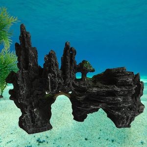 Puede incluir: Decoración de acuario gris oscuro que representa una cordillera rocosa con arcos y un pequeño árbol. La formación rocosa artificial es texturizada y se asienta sobre un fondo arenoso, con un fondo azul que sugiere un entorno submarino.