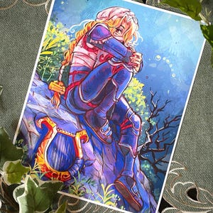 May include: A rectangular art print featuring a digital illustration of a blonde character with long hair, wearing blue and white armour, sitting on a rock. A golden lyre with red accents rests on the rock beside the character against a blue background.