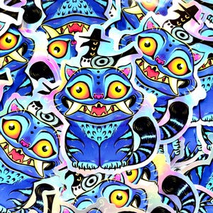 May include: A collection of blue cat stickers with a cartoon design. The cats have large yellow eyes, sharp teeth, and black striped tails. The stickers have a holographic effect, with pink and yellow highlights.