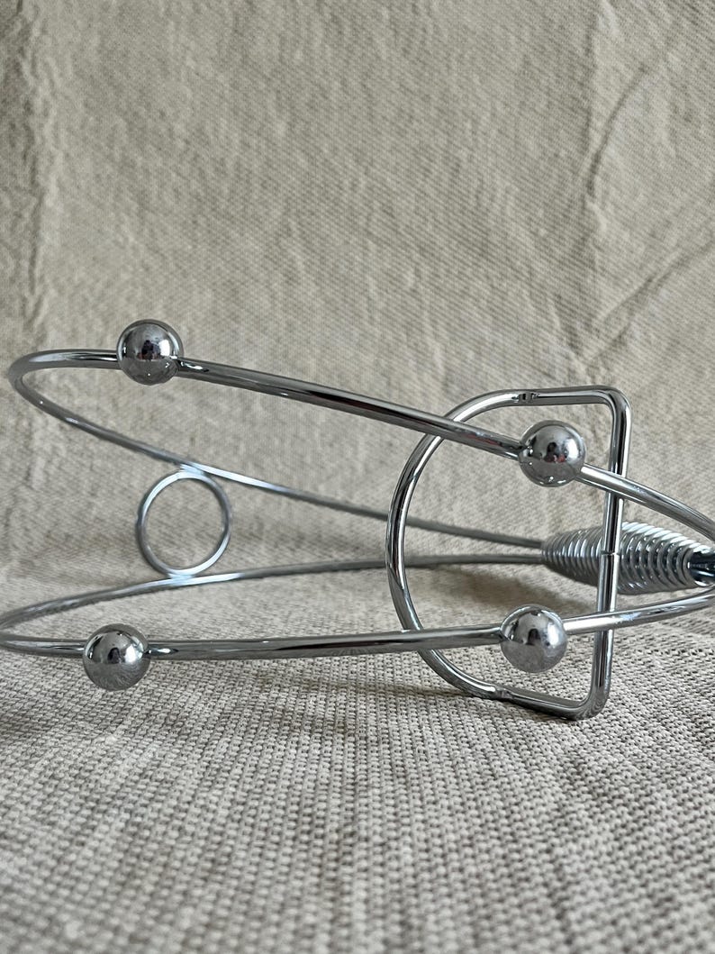 May include: A chrome wine bottle holder with a contemporary design. It has a circular base, curved metal bars, and four small spherical accents. The holder's design is sleek and minimalist, suitable for displaying wine bottles.