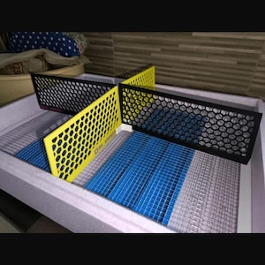 Può includere: Struttura rettangolare con motivo a nido d'ape, divisa in sezioni con pannelli neri e gialli. La base presenta una rete blu e grigia. Il design suggerisce un sistema di ventilazione o filtrazione.