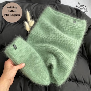 May include: A fuzzy, light green knitted cowl and matching beanie set with a visible texture. The items feature a small dark tag with white text. A circular graphic in the top left corner contains the text Knitting Patten PDF English.