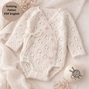 Könnte beinhalten: Ein weißer, langärmeliger, gestrickter Babybody mit einem zarten rautenförmigen Spitzenmuster, einer Wickeloptik mit kleinen Knöpfen und einem seitlichen Bindeband. Das Bild enthält den Text Knitting Patten PDF English.