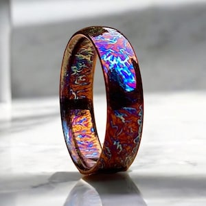 May include: A close-up of a colorful, iridescent metal ring. The ring has a unique, swirling pattern of blue, purple, and orange hues.