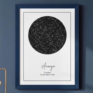 Peut inclure: Une affiche encadrée avec une carte du ciel en noir et blanc, dans un cadre blanc et bleu marine. L'affiche affiche le nom "Ananya" et les détails de localisation et de date. L'affiche est accrochée à un mur bleu marine.