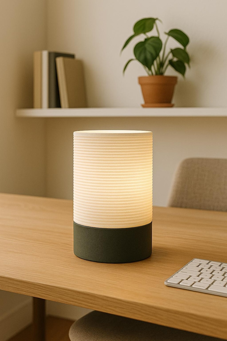 Puede incluir: Una l&aacute;mpara de mesa cil&iacute;ndrica blanca y verde con una pantalla blanca acanalada y una base verde oscuro. La l&aacute;mpara est&aacute; sobre una mesa de madera con un teclado.