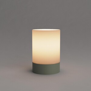 Puede incluir: Una l&aacute;mpara de mesa blanca con una pantalla de vidrio acanalada y una base verde.