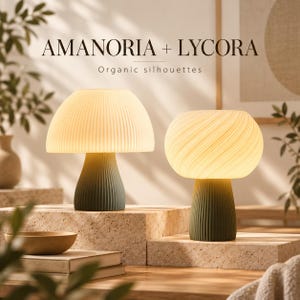 Op de afbeelding: Twee paddestoelvormige tafellampen met het opschrift AMANORIA + LYCORA Organic silhouettes. De linkerlamp heeft een cr&egrave;mekleurige geplooide kap en een donkergroene voet. De rechterlamp heeft een wervelende cr&egrave;mekleurige kap.
