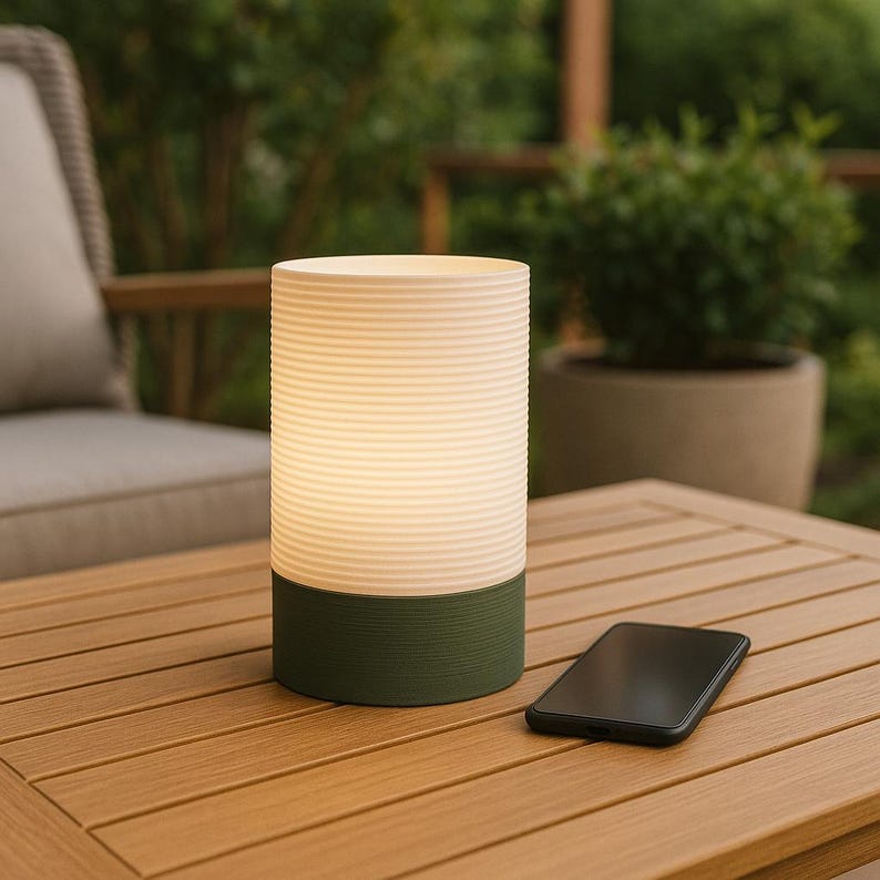 Puede incluir: Una l&aacute;mpara cil&iacute;ndrica blanca y verde con un dise&ntilde;o acanalado se encuentra sobre una mesa de madera. Un tel&eacute;fono inteligente negro est&aacute; sobre la mesa junto a la l&aacute;mpara.