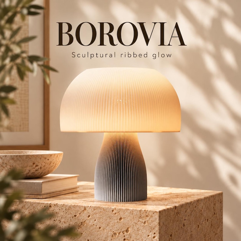 Op de afbeelding: Een tafellamp met een paddenstoelvormige, geribbelde witte kap en een taps toelopende, geribbelde grijze voet. De tekst BOROVIA Sculptural ribbed glow is boven de lamp zichtbaar. De lamp verspreidt een warm, zacht licht over de textuur.