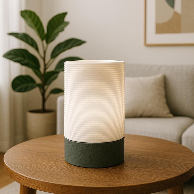 Puede incluir: Una l&aacute;mpara de mesa blanca y gris con una pantalla blanca texturizada y una base gris oscuro. La l&aacute;mpara est&aacute; sobre una mesa de madera.