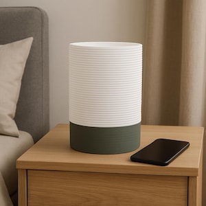 Puede incluir: Un jarr&oacute;n cil&iacute;ndrico de cer&aacute;mica blanco y verde con textura acanalada. El jarr&oacute;n est&aacute; sobre una mesita de noche de madera con un tel&eacute;fono m&oacute;vil en la superficie.