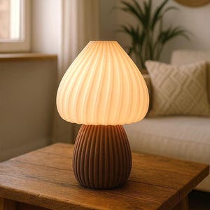 May include: A mushroom-shaped table lamp with a ribbed, brown base and a cream-colored, ribbed shade. The lamp sits on a wooden table, providing soft, ambient lighting. The design is modern and decorative, suitable for home decor.