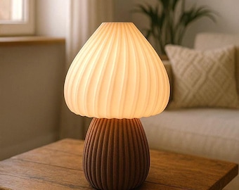 May include: A mushroom-shaped table lamp featuring a translucent, ribbed, off-white glass shade that emits a soft glow, resting on a dark brown, vertically fluted cylindrical base. The lamp has a distinct two-part design with a rounded top.