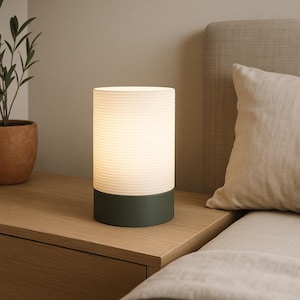 Puede incluir: Una l&aacute;mpara de mesita de noche blanca con una base verde y una pantalla de vidrio acanalada. La l&aacute;mpara est&aacute; encendida e ilumina la habitaci&oacute;n.