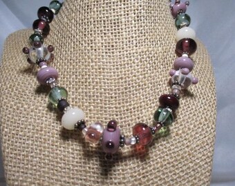 A Hand Crafted Lamp Work Bead Choker Necklace in Shades of Purple, White and Green w/Sparkling Rhinestone Accents.