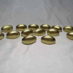 May include: A collection of oval-shaped, gold-colored cabinet pulls. The hardware has a smooth, metallic finish and a slightly curved design. The pulls are arranged on a white surface, suggesting a home decor or DIY theme.