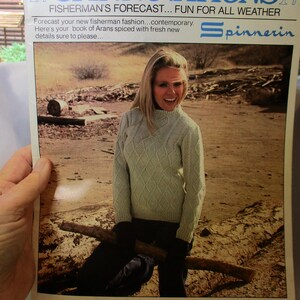 May include: A vintage Spinnerin knitting pattern booklet titled 14 SPINNOVATIONS FISHERMAN'S FORECAST... FUN FOR ALL WEATHER. The cover features a photograph of a person wearing a light-colored, long-sleeved, diamond-patterned cable knit sweater.