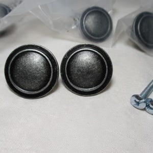 May include: Set of antique-style cabinet knobs with a distressed, metallic finish. The knobs are round with a raised center and a decorative outer ring. Includes mounting screws. Ideal for furniture restoration or DIY projects.