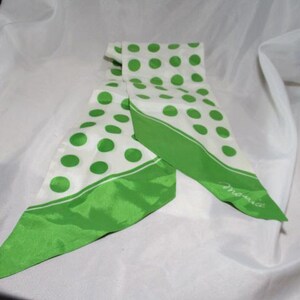 May include: A white scarf with large green polka dots and a solid green border. The scarf is folded and has a pointed end. The word "Monique" is written in cursive on the end of the scarf.