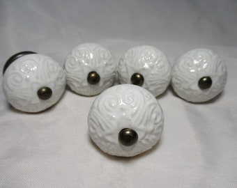 A Set of Five White Ceramic Knobs with Embossed Scrollwork designs on the Top & Antiqued Brass Hardware.