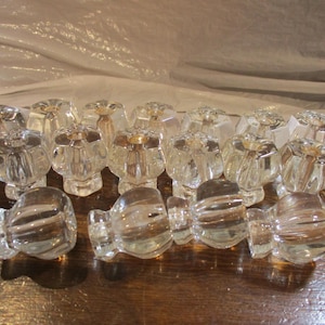 May include: A collection of clear glass cabinet knobs featuring a multi-faceted, hexagonal design with a smooth, rounded top surface. Each knob has a sturdy base and a reflective, transparent finish that catches light, creating a uniform appearance.
