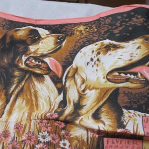 May include: A vintage textile featuring two dogs with their tongues out. The dogs are set against a backdrop of trees and flowers. The textile has a pink border and a calendar in French.