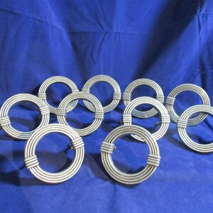 May include: A collection of nine circular metal drawer pulls, each featuring a series of concentric rings and two horizontal banded accents on opposite sides. The hardware has a matte silver finish and a consistent, repeating grooved design.
