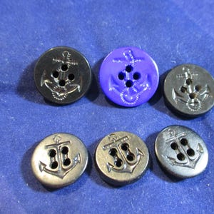 May include: A set of six round buttons, each featuring a molded anchor design and four holes for attachment. Five of the buttons are black, while one button is a vibrant purple. The buttons have a smooth, glossy finish and a raised anchor motif.