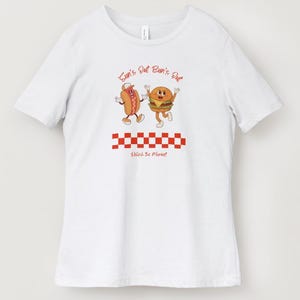 May include: White t-shirt featuring a cartoon hot dog and hamburger with arms and legs, and the text "Sun's Out Bun's Out". Below the characters is a red and white checkered pattern and the text "Relish the Moment".