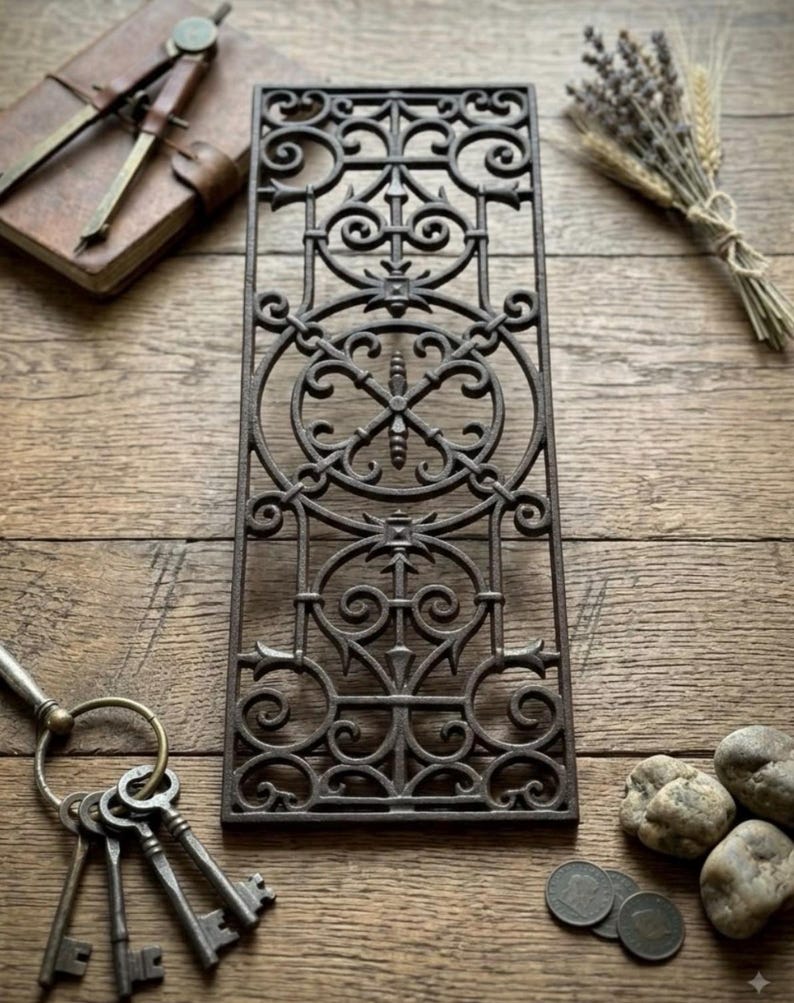 May include: A rectangular cast iron grate featuring an intricate openwork pattern of symmetrical scrolls, circles, and pointed finials. The metal surface has a dark, weathered finish with a repeating geometric design throughout the panel.