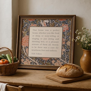 Può includere: Una stampa incorniciata con una citazione di J.R.R. Tolkien su una casa, su uno sfondo a motivi floreali nei toni dell'arancione e del blu. La stampa è appoggiata su un tavolo di legno accanto a un cesto di vimini con verdure e un pane.