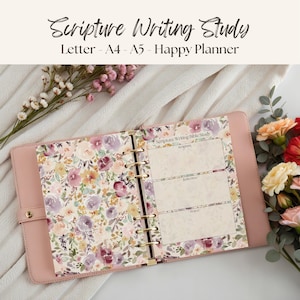May include: A pink planner with gold rings and a floral design. The planner is open, revealing pages with floral patterns and sections for scripture, reflection, and prayer. The text "Scripture Writing Study" is at the top.