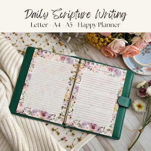 Könnte beinhalten: Offenes grünes Lederjournal mit linierten Seiten und floralem Rand. Das Journal ist geöffnet, um die linierten Seiten mit den Worten "Daily Scripture Writing" oben zu zeigen. Das Journal liegt auf einer weißen Oberfläche mit Blumen.