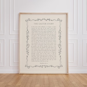 Puede incluir: Impresión enmarcada con el texto "THE EASTER STORY" en un borde decorativo. El texto es negro sobre un fondo crema. El marco es de color madera clara, y la impresión se muestra sobre un suelo de madera.