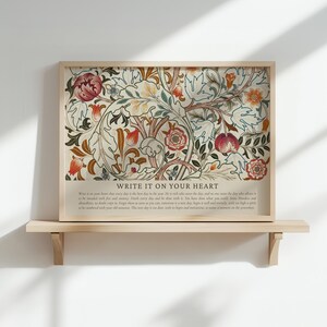 May include: A framed floral art print with a beige background and a wooden frame. The print features a colorful botanical design with red, orange, and green flowers and leaves. The text "WRITE IT ON YOUR HEART" is at the bottom.