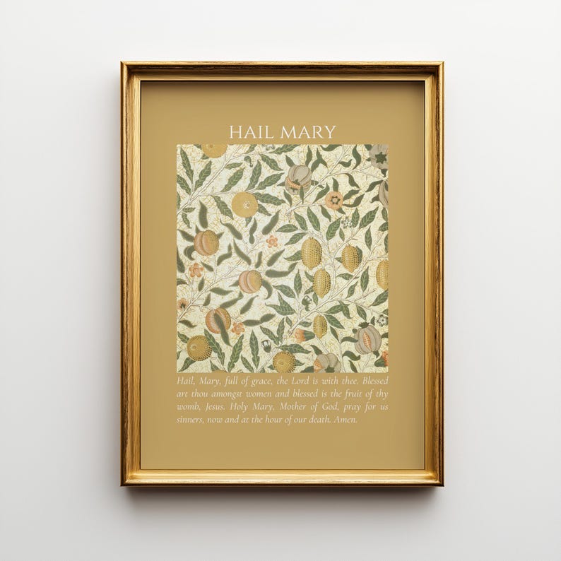 May include: A framed wall art print featuring a gold border and a central botanical pattern of green leaves and tan fruits on a cream background. The text HAIL MARY appears at the top, with the full Hail Mary prayer printed in white at the bottom.