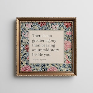 May include: A square framed wall art piece featuring a quote by Maya Angelou that reads, There is no greater agony than bearing an untold story inside you. The text is centered on a beige background surrounded by a dark blue floral pattern.