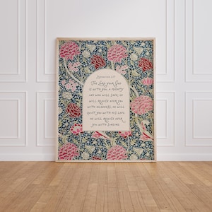 Puede incluir: Un estampado enmarcado con un diseño floral en tonos rosa, rojo y azul. El estampado incluye el texto "Sofonías 3:17" y una cita sobre el amor y el regocijo de Dios. La obra de arte se exhibe sobre un suelo de madera.