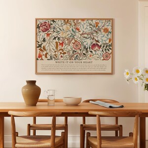 May include: A framed floral art print with a beige background and a variety of flowers in shades of red, orange, and green. The print is above a wooden table with a vase, a glass, and a bowl. The text "WRITE IT ON YOUR HEART" is at the bottom of the print.